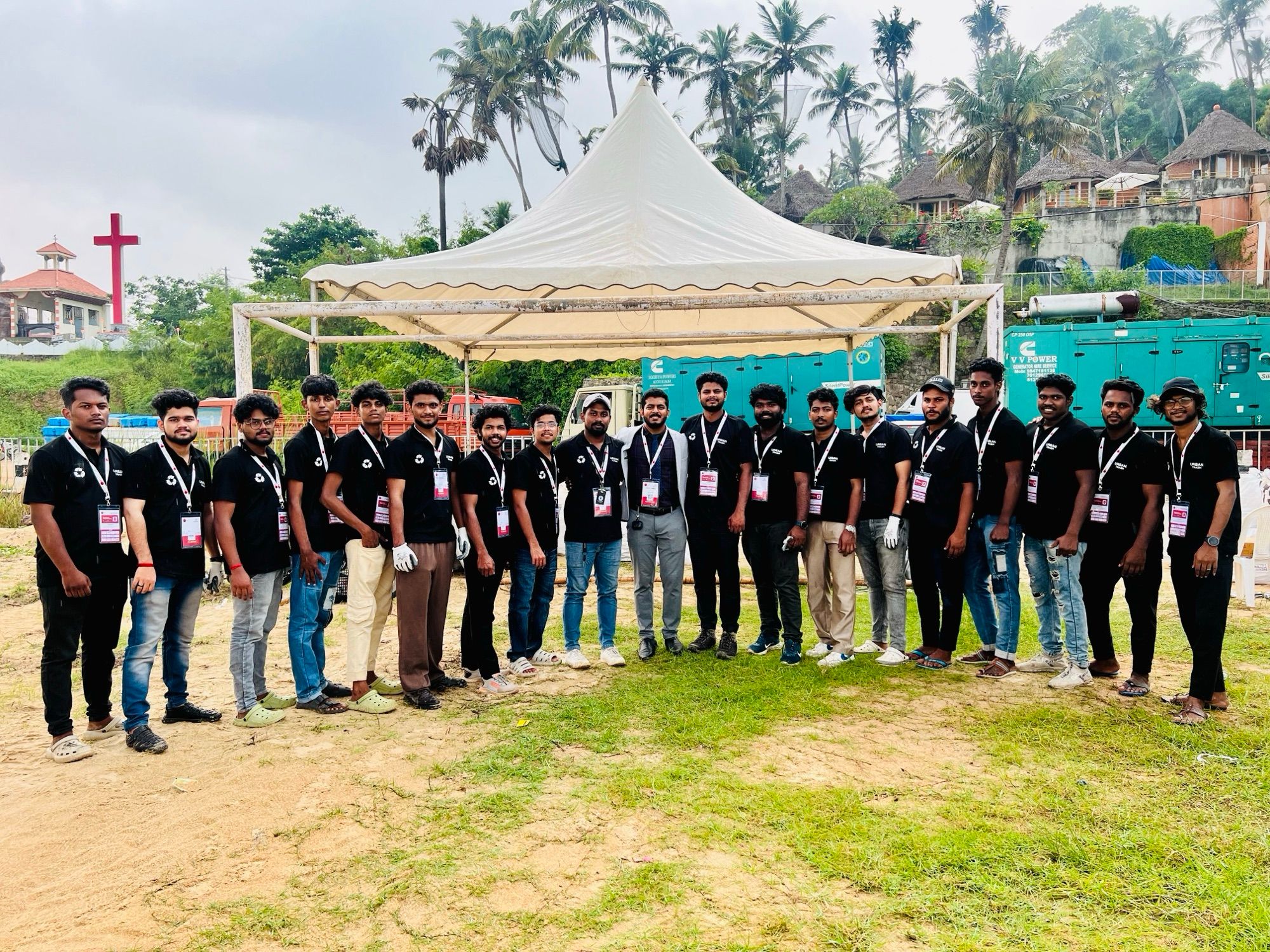Nearly twenty team members in black polo shirts stand in a line in front of a white tent, with a man in a grey jacket in the middle.